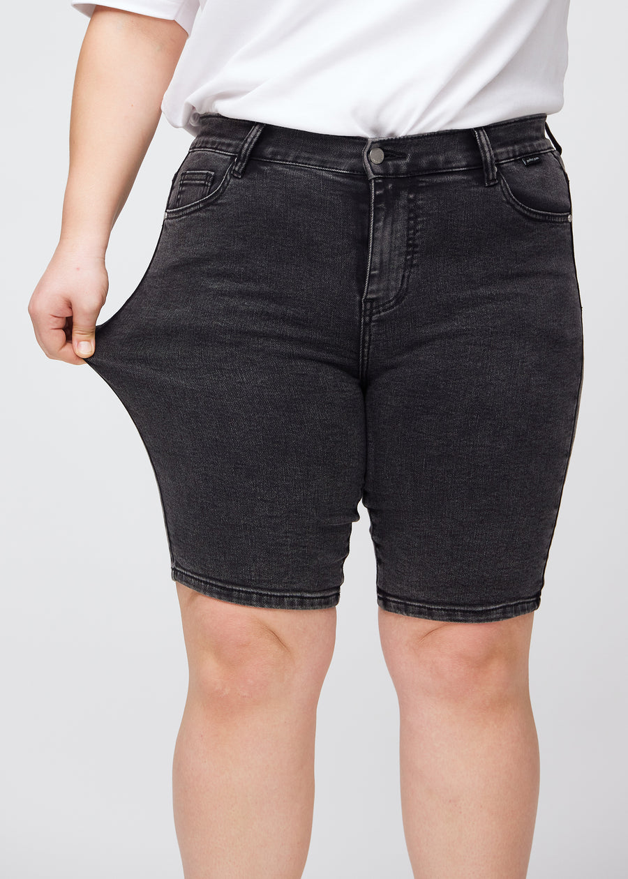 Plus-size model strækker shortsene ved låret for at vise stretch.