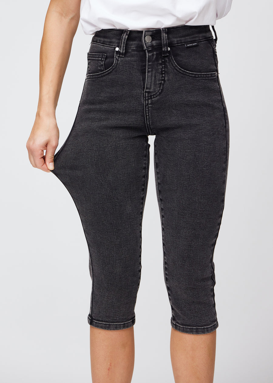 Model strækker caprisene ved låret for at vise det bløde og fleksible stretch i den mørkegrå denim.