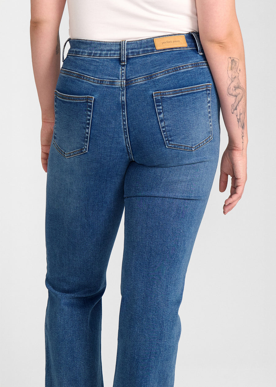Mørkeblå denim bootcut jeans, modelnavn Oceans, som sidder tæt om hofter og lår med et let svaj fra knæet og ned, set bagfra tæt på for at vise detaljer. på en plus-size model.