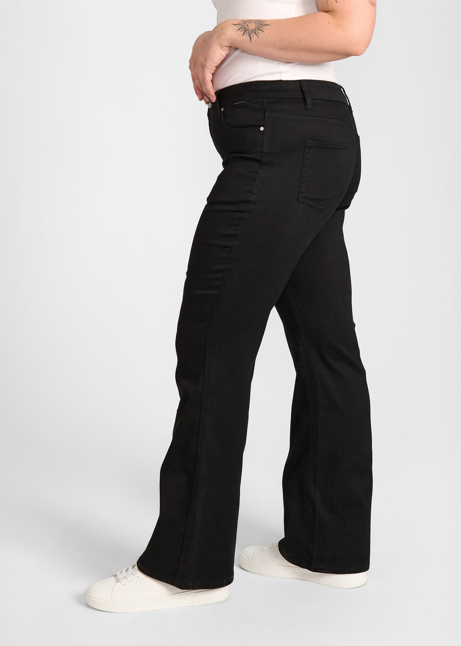 Sort bootcut jeans, modelnavn Ravens, som sidder tæt om hofter og lår med et let svaj fra knæet og ned, set fra siden på model på en plus-size model.