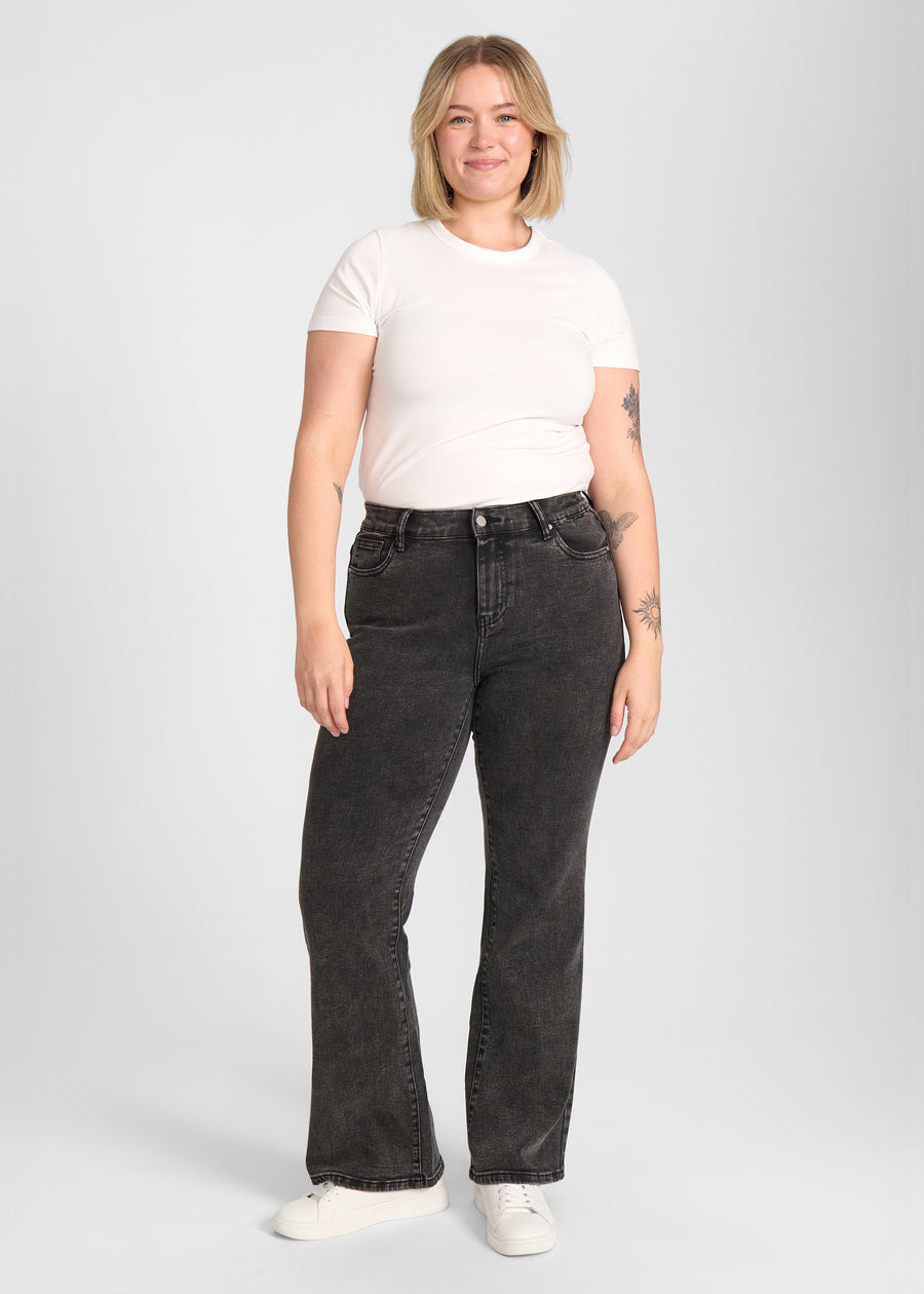 Fuldt billede af model i mørkegrå denim bootcut jeans på en plus-size model.