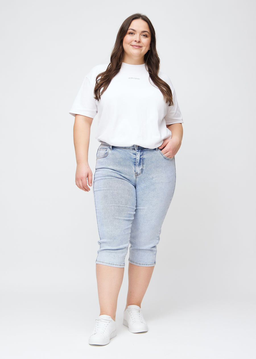 Plus-size model går ind i billedet, strækker i sine lyseblå denim slim capris, drejer rundt for at vise dem frem og forlader derefter billedet.