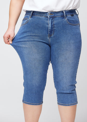 Plus-size model viser stretch ved at trække i caprisene ved låret – fokus på komfort og fleksibilitet i den blå denim.