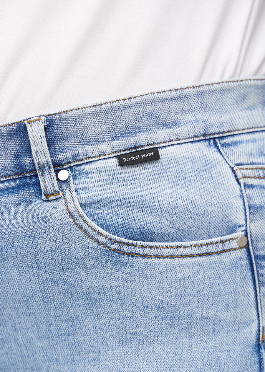 Close-up of light blue denim with Perfect Jeans logo label at the front pocket edge, on a plus-size model.
