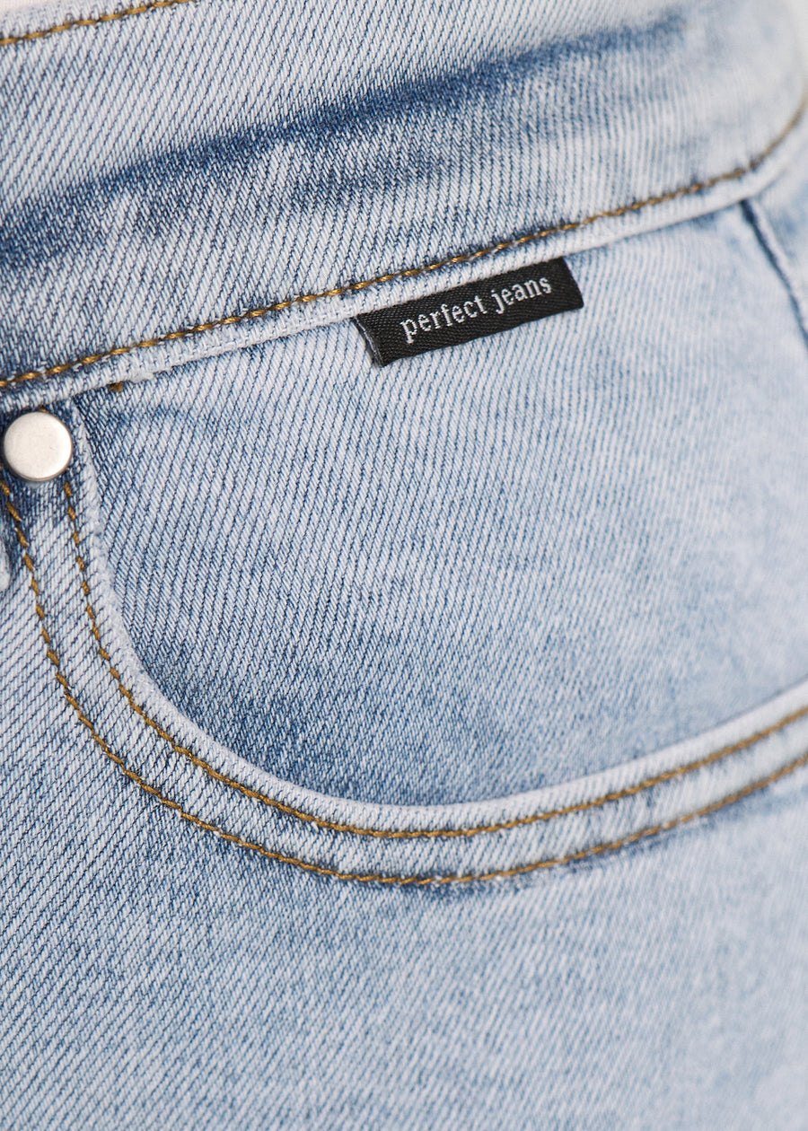Nærbillede af lyseblå denim med Perfect Jeans logoetiket ved forlommekanten, på en plus-size model.