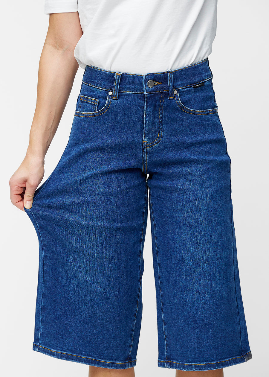 Model strækker de løse, mørkeblå denim capris i farven Oceans ved hoften for at vise materialets stretch.