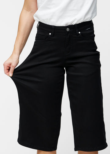 Model strækker de løse, sorte capris i farven Ravens ved hoften for at vise materialets stretch.