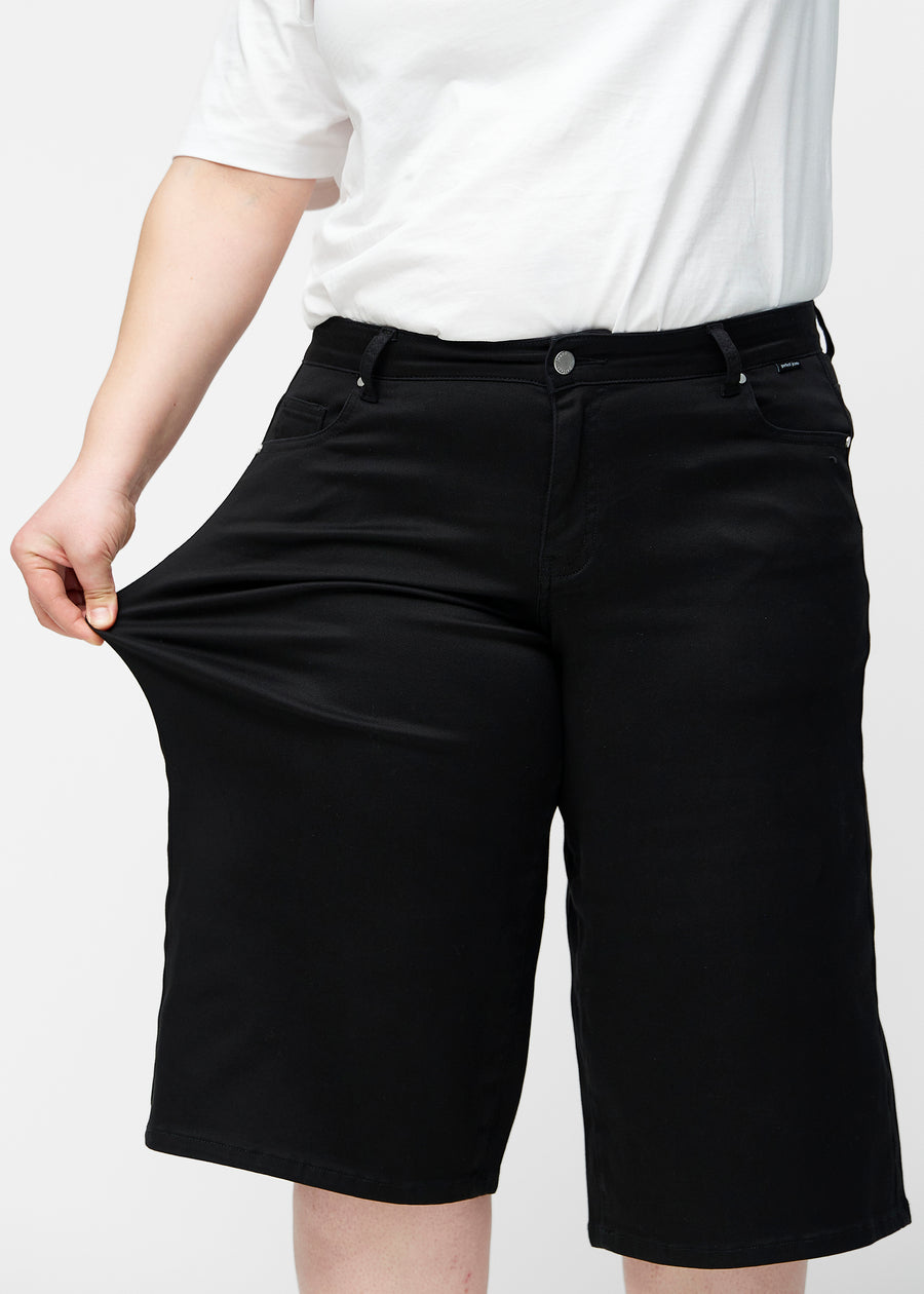 Plus-size model strækker de løse, sorte capris i farven Ravens ved hoften for at vise materialets stretch.