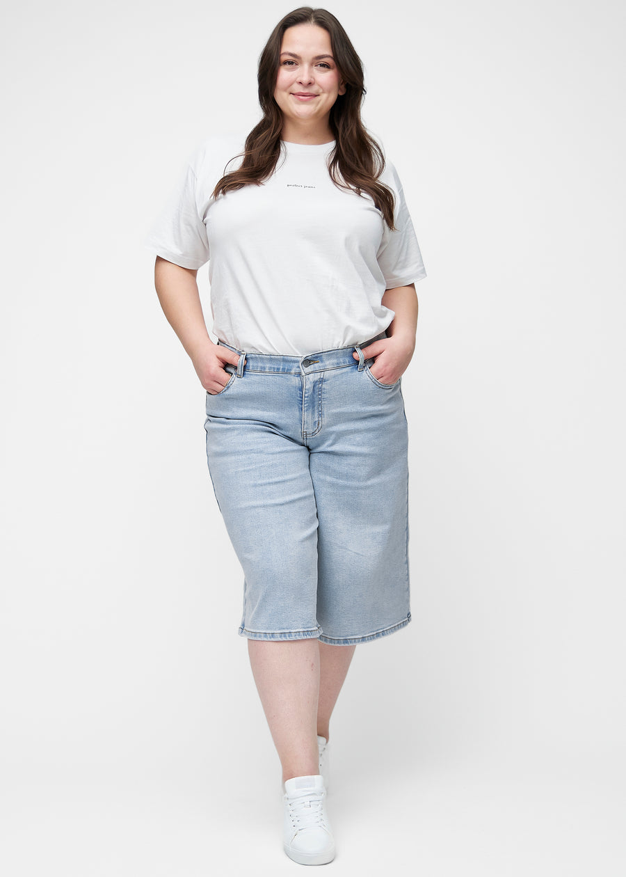Full image of a plus-size model wearing loose, light blue denim capris in the colour Waves, reaching just below the knee.