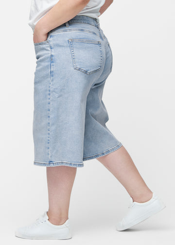 Loose, light blue denim capris in the colour Waves seen from the side on a plus-size model, where the wide fit and length to just below the knee are visible.