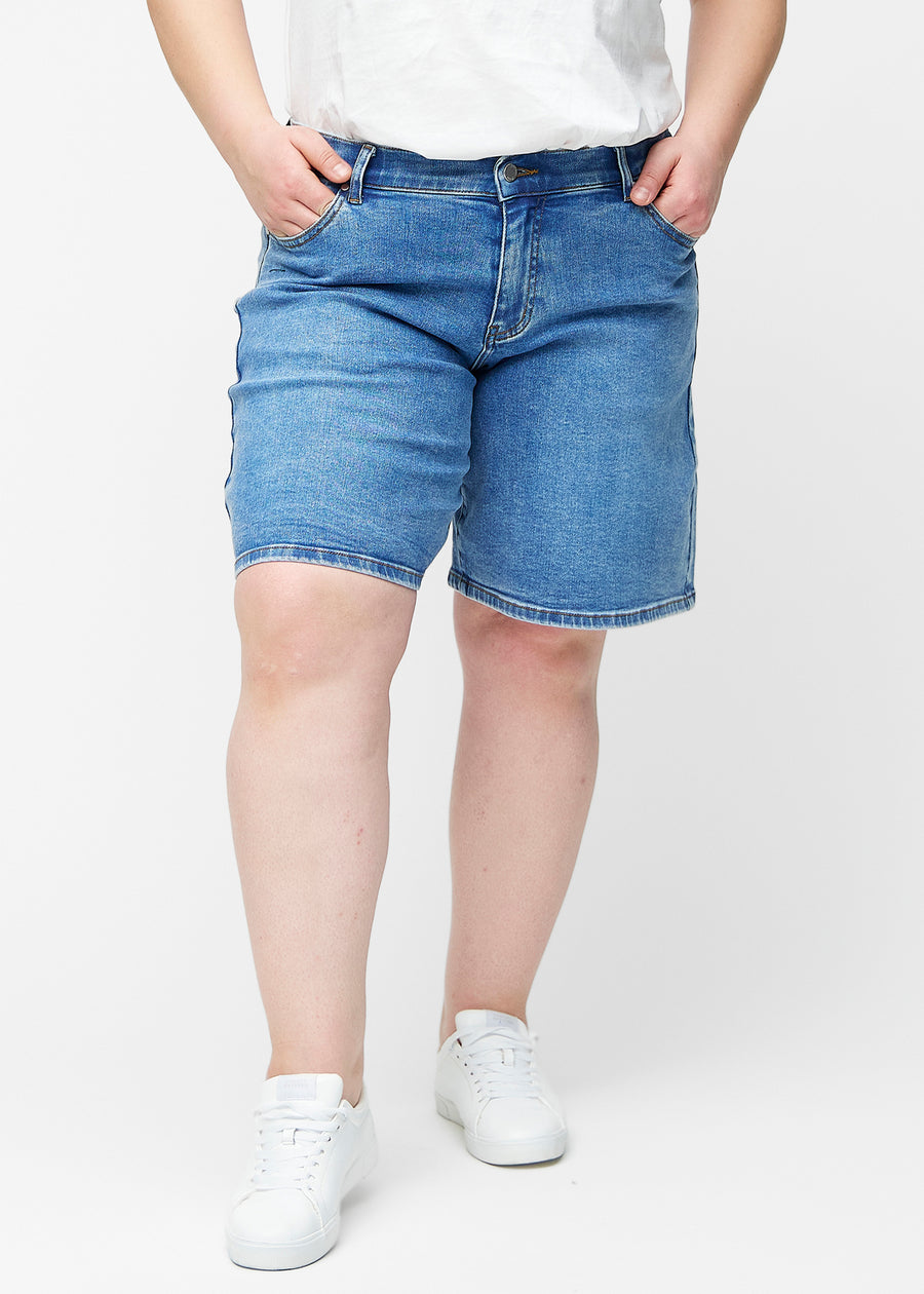 Løse, klassisk blå denim shorts i farven Rivers set forfra på plus-size model, der sidder til ved hoften og falder løst ned.
