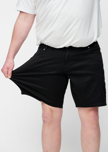 Plus-size model stretches the black shorts for men in the colour Ravens at the thigh to show the stretch of the material.