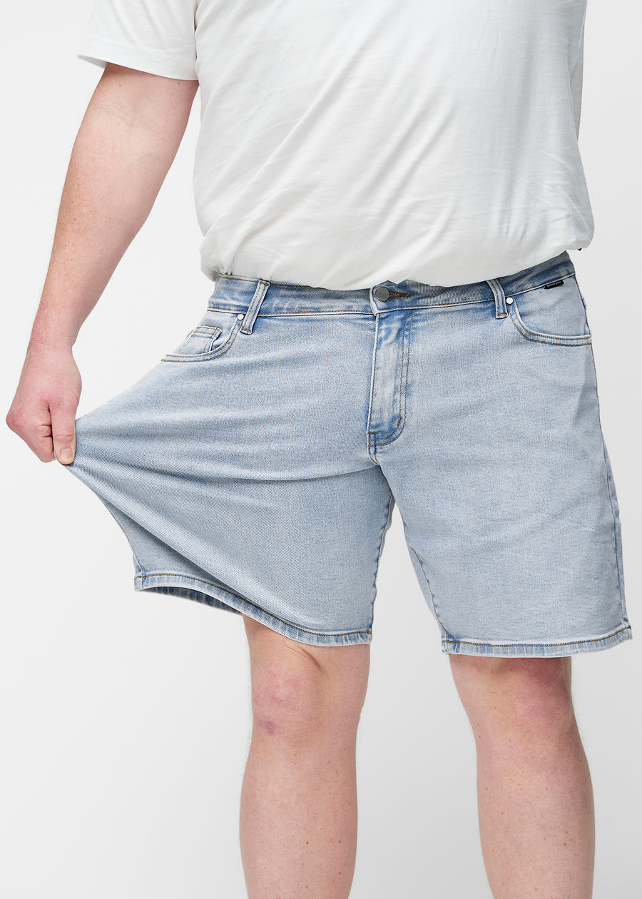 Plus-size model stretches light blue denim shorts for men in the colour Waves at the thigh to show the material’s stretch.