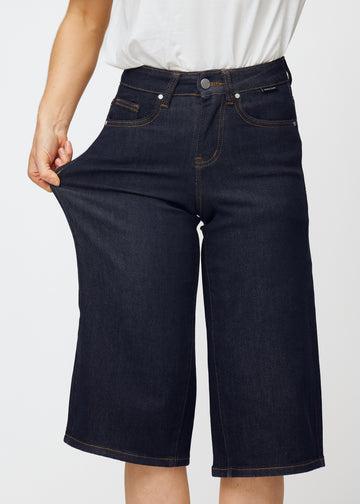 Model stretches deep dark blue denim capris for women in the colour Midnights at the thigh to show the material’s stretch.
