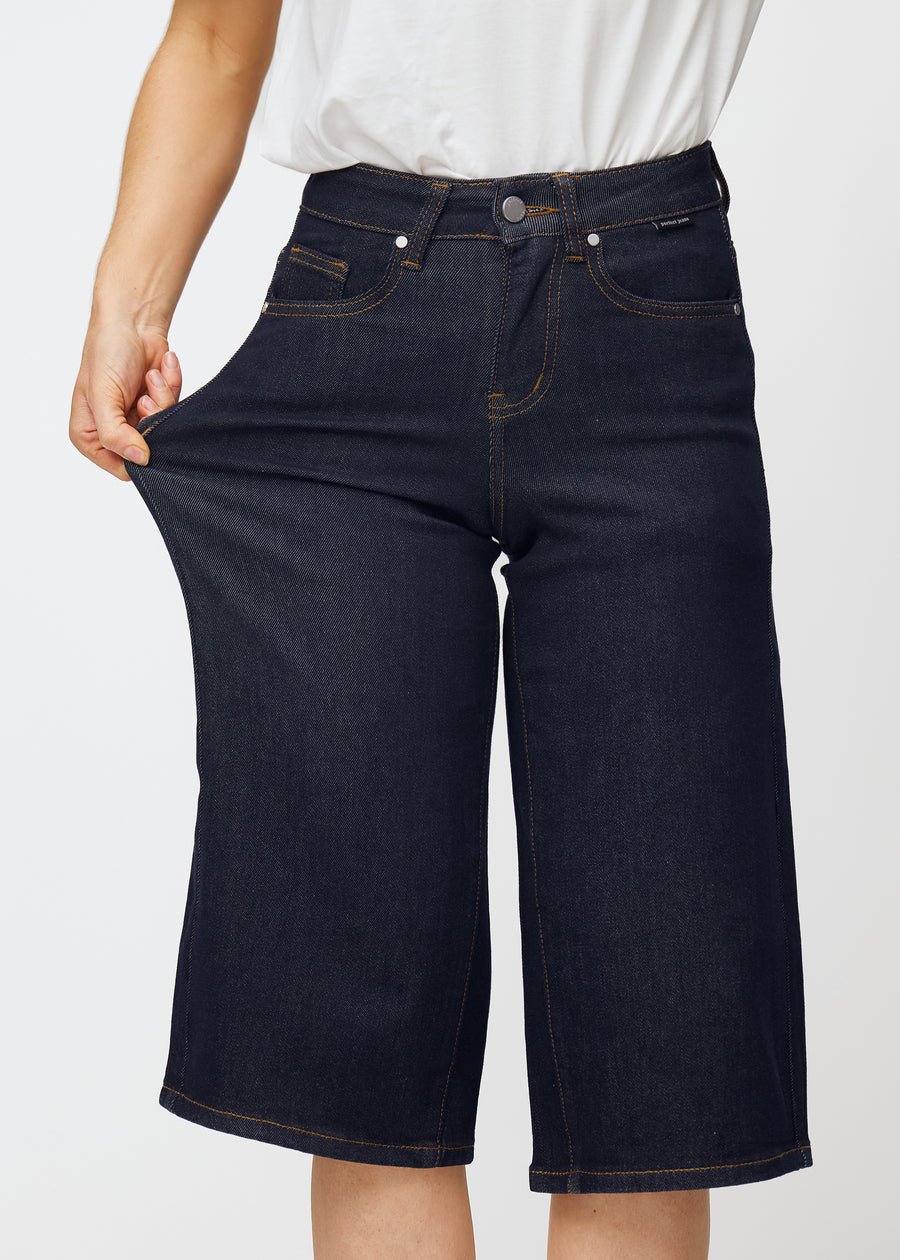 Model stretches deep dark blue denim capris for women in the colour Midnights at the thigh to show the material’s stretch.