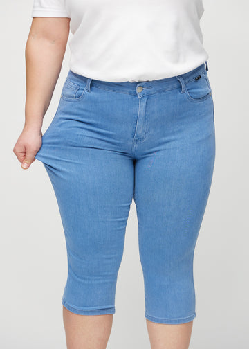 Skinny capris for women in blue fabric, color Geraniums. A plus-size model stretches the fabric to demonstrate its flexibility.