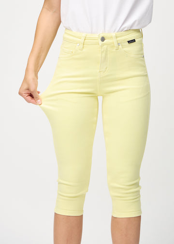 Skinny capris for women in pastel yellow fabric, color Lemonades. A model stretches the fabric to demonstrate its flexibility.