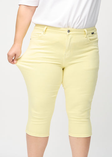 Skinny capris for women in pastel yellow fabric, color Lemonades. A plus-size model stretches the fabric to demonstrate its flexibility.