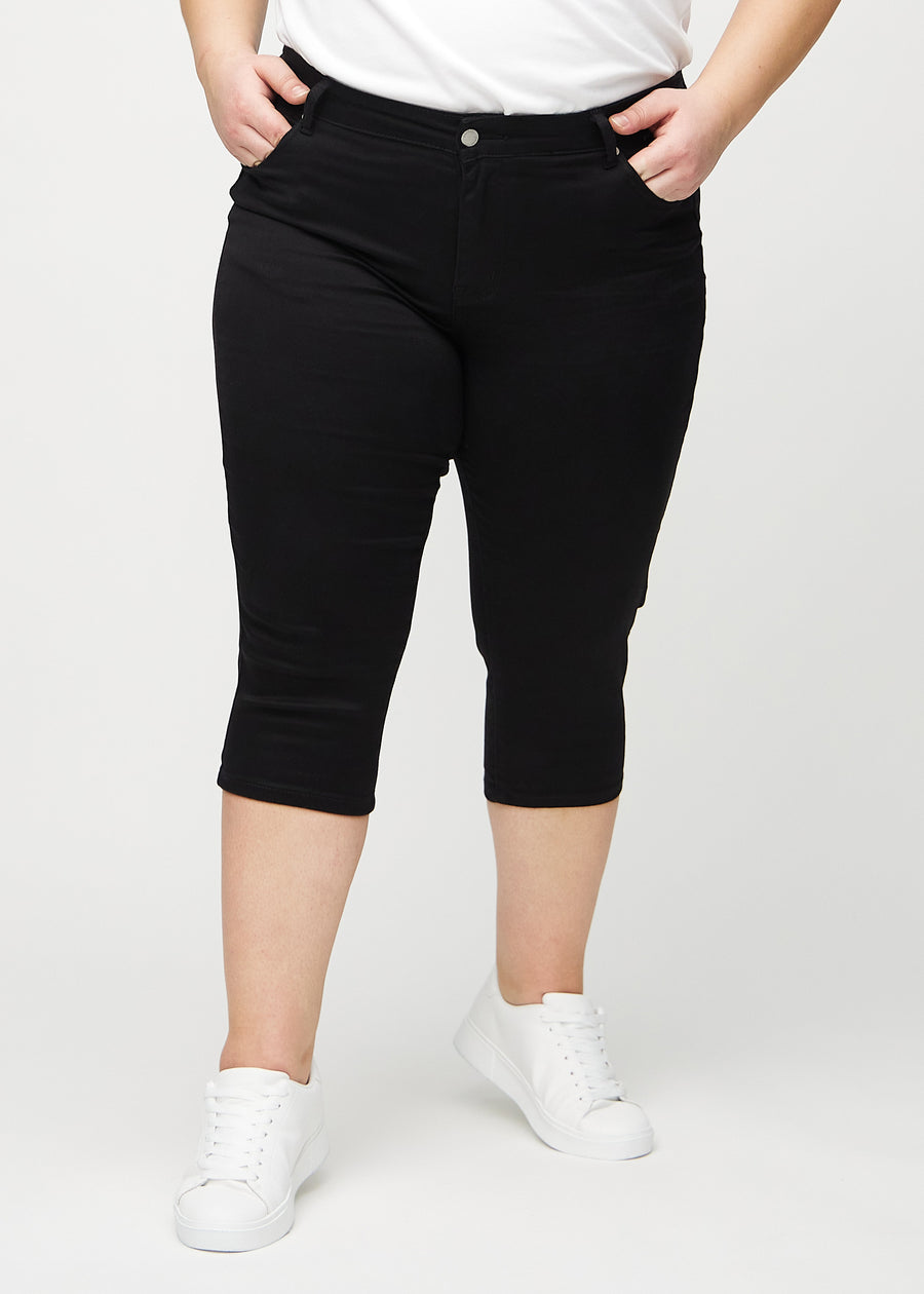 Skinny capris for women in black fabric, color Ravens. Front view on a plus-size model, showing the close-fitting legs ending just below the knee.