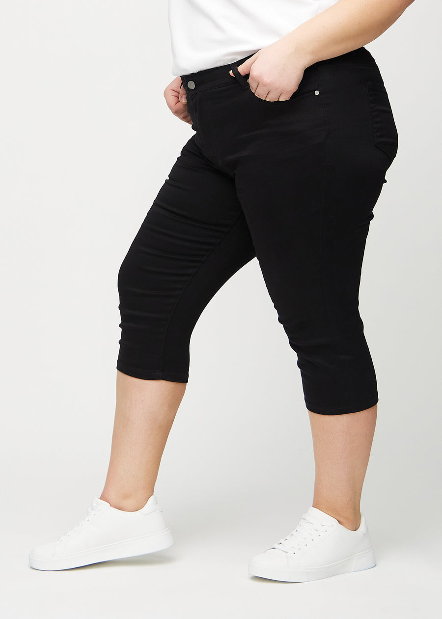 Skinny capris for women in black fabric, color Ravens. Side view on a plus-size model, showing the fitted cut.