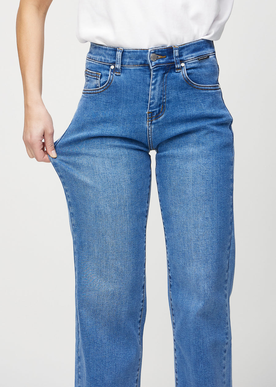 Loose jeans for women in blue, color Rivers. A model stretches the denim at the thigh to show the fabric&