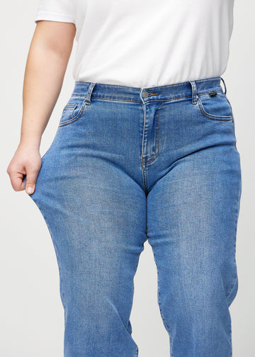 Loose jeans for women in blue, color Rivers. A plus-size model stretches the denim at the thigh to show the fabric&