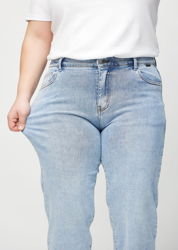 Loose jeans for women in light blue, color Waves. A plus-size model stretches the denim at the thigh to show the fabric&