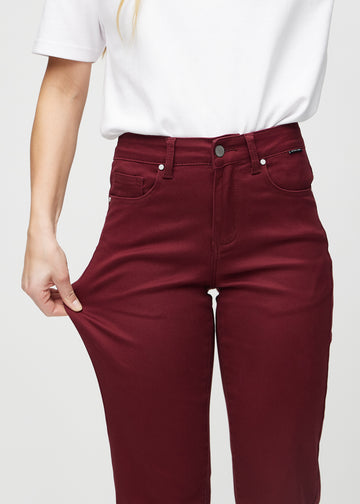 Regular jeans for women in dark red, color Santas. A model stretches the fabric at the thigh to show its stretch.