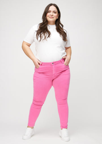 Skinny jeans for women in light pink, color Flamingos. Full-length view of a plus-size model in the jeans.