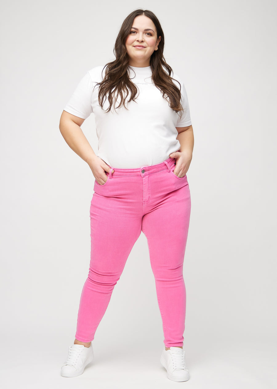 Skinny jeans for women in light pink, color Flamingos. Full-length view of a plus-size model in the jeans.