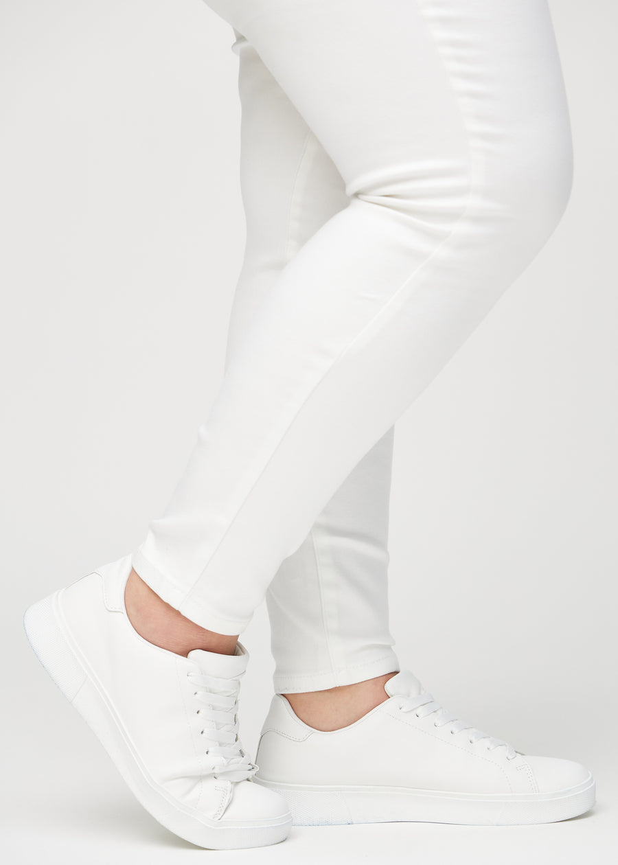 Skinny jeans for women in white, color Marguerites. Close-up of the snug-fitting leg openings at the ankles on a plus-size model.