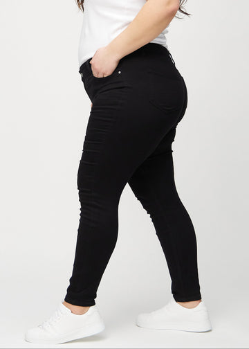 Skinny jeans for women in black, color Ravens. Side view on a plus-size model.
