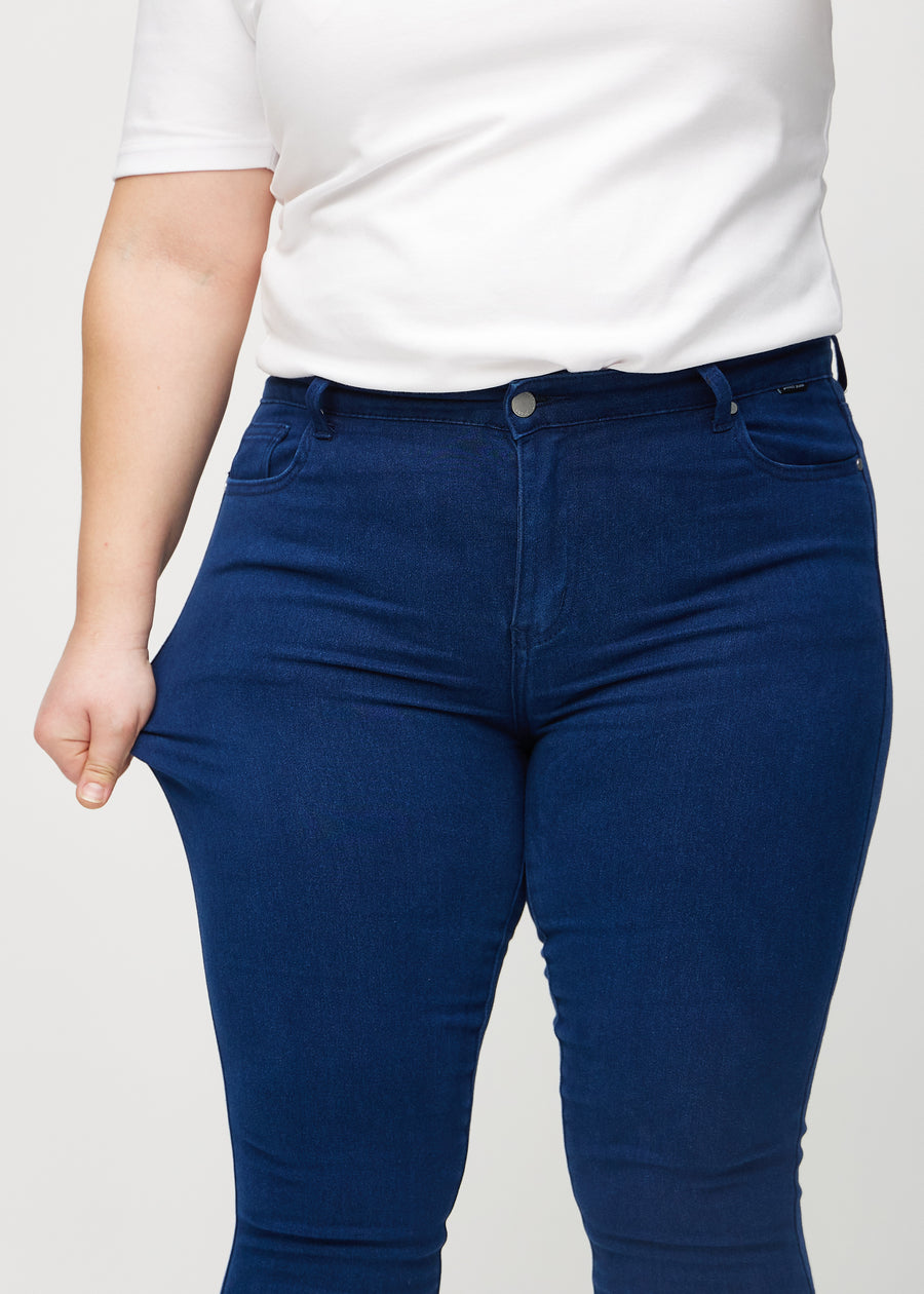 The plus-size model stretches the jeans at the thigh to show the stretch.