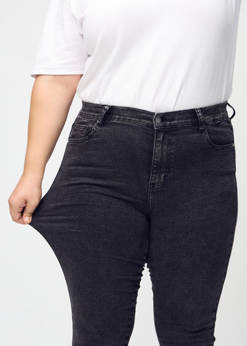 The plus-size model stretches the jeans at the thigh to show the stretch.