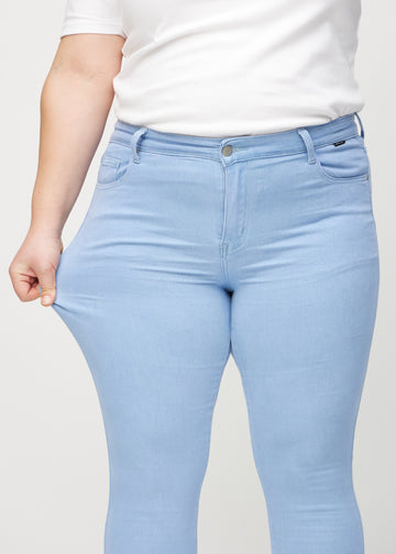 Skinny jeans for women in light blue, color Skies. A plus-size model stretches the jeans at the thigh to show the fabric&