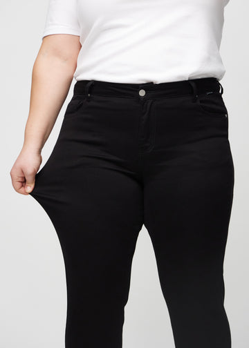 Slim jeans for women in black, color Ravens. A plus-size model stretches the jeans at the thigh to show the fabric&