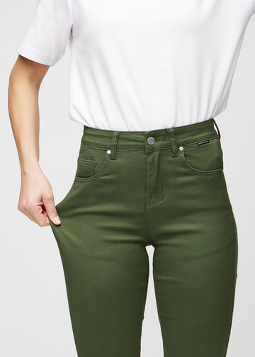 Slim jeans for women in dark green, color Renewals. A model stretches the jeans at the thigh to show the fabric&