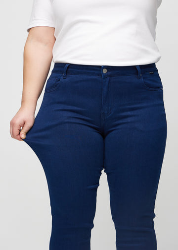 Slim jeans for women in dark blue, color Royals. A plus-size model stretches the jeans at the thigh to show the fabric&