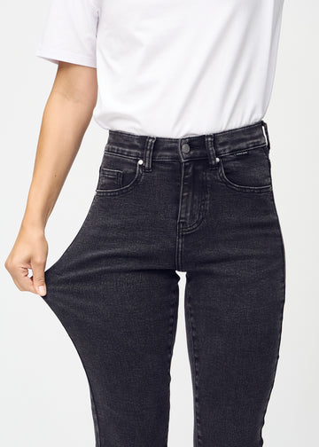 Slim jeans for women in dark grey, color Shadows. A model stretches the jeans at the thigh to show the fabric&