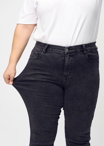 Slim jeans for women in dark grey, color Shadows. A plus-size model stretches the jeans at the thigh to show the fabric&
