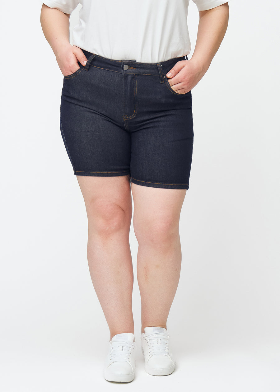 Deep dark blue denim shorts for women in the colour Midnights with a skinny fit seen from the front on a plus-size model.
