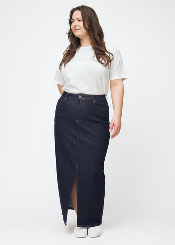 Full image of a plus-size model wearing a long deep dark blue denim skirt for women in the colour Midnights with a front slit.