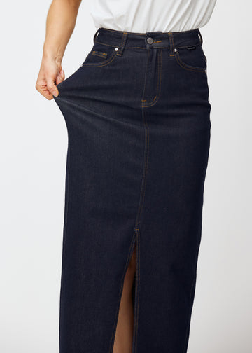 Model stretches the long deep dark blue denim skirt for women in the colour Midnights at the hip to show the material’s stretch.