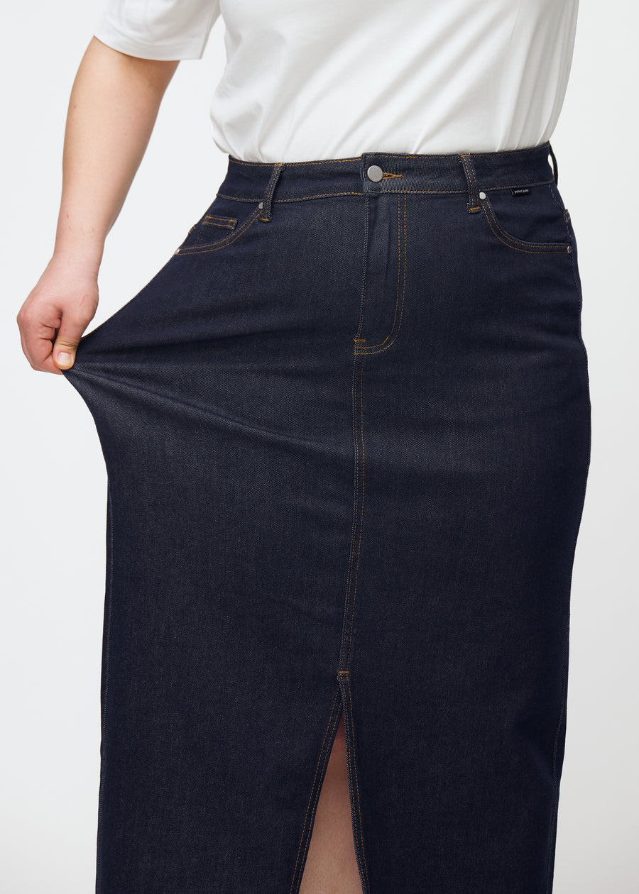 Plus-size model stretches the long deep dark blue denim skirt for women in the colour Midnights at the hip to show stretch.