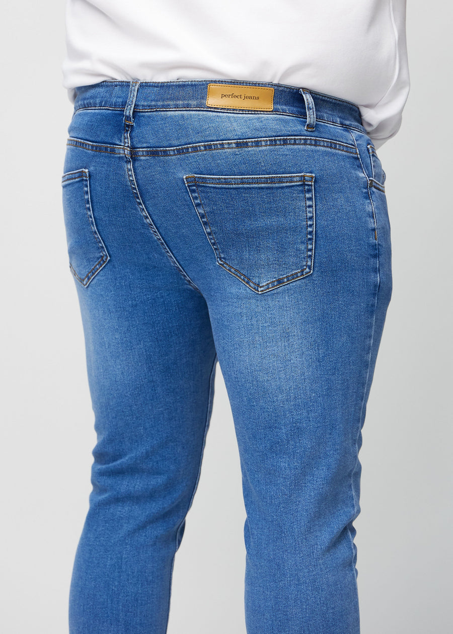 Close-up back view of blue denim slim jeans on a plus-size model showing details.