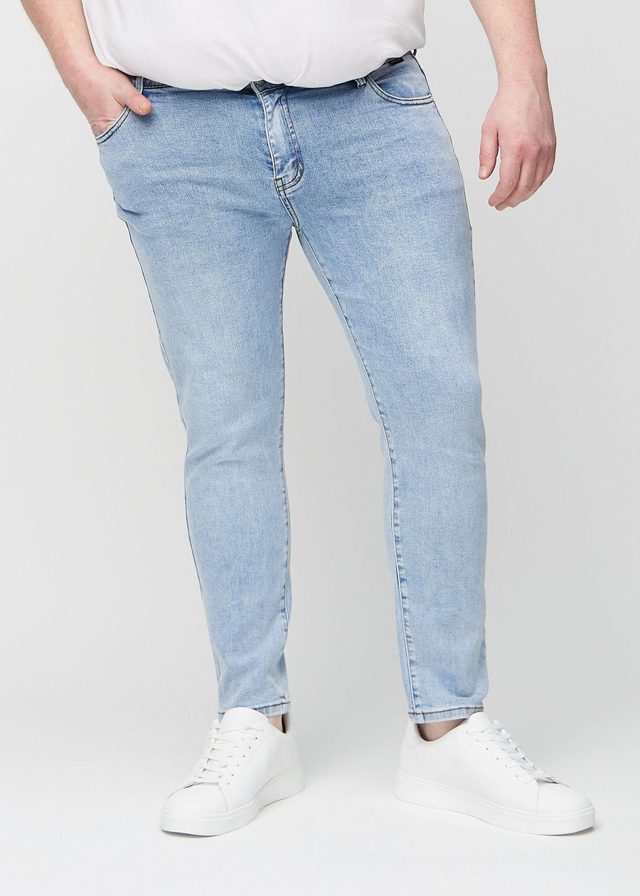 Light blue denim slim jeans, model name Waves, fitted closely along the legs on a plus-size model, front view.