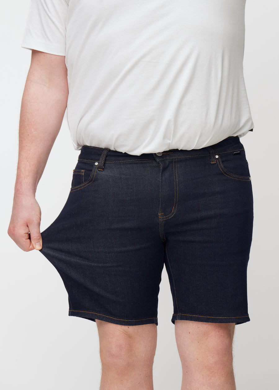 Plus-size model stretches deep dark blue denim shorts for men in the colour Midnights at the thigh to show stretch.