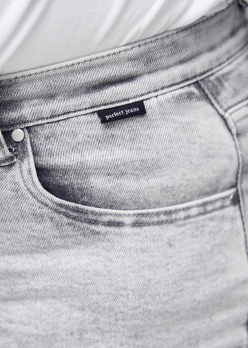 Detaljebillede af forlommen på de lysegrå denim i farven Ashes – logo og snit fremhævet på plus-size model.