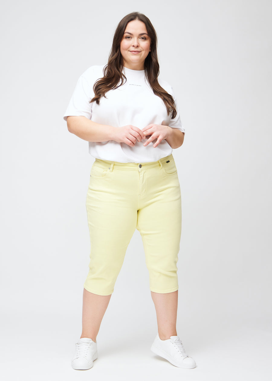 Fuldt billede af plus-size model i lysegule slim capris.
