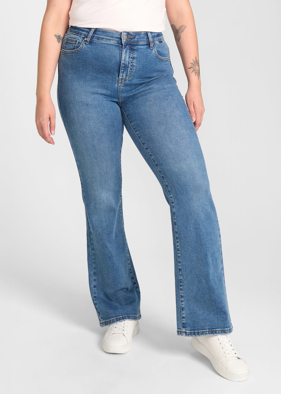 Blå denim bootcut jeans, modelnavn Rivers, som sidder tæt om hofter og lår med et let svaj fra knæet og ned, set forfra på en plus-size model.
